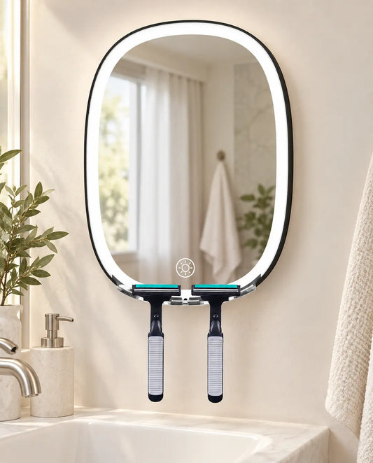 Black oval LED shaving mirror with two razors on its clear holder above a bathroom sink.