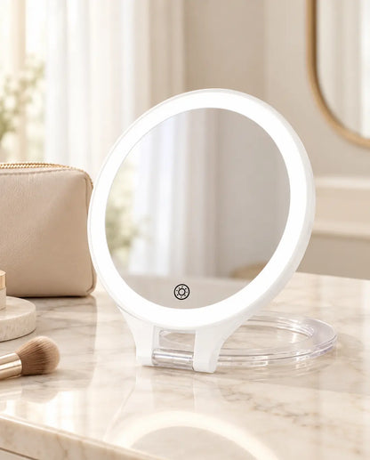 White round LED travel mirror with a black touch control and transparent folding ring base.